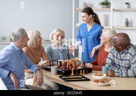 Gruppo di anziani felici che giocano a scacchi in un ambiente sanitario, impegnati e socializzanti insieme Foto Stock