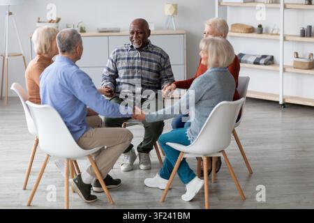 Sessione di terapia di gruppo con anziani diversificati, tenendosi per mano, condividendo emozioni, ambiente interno Foto Stock