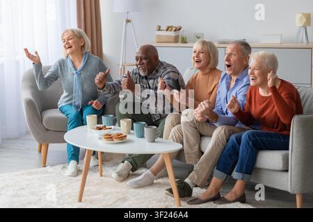 Gruppo diversificato e felice di anziani che guardano una partita e tifano insieme a casa, emozione gioiosa Foto Stock