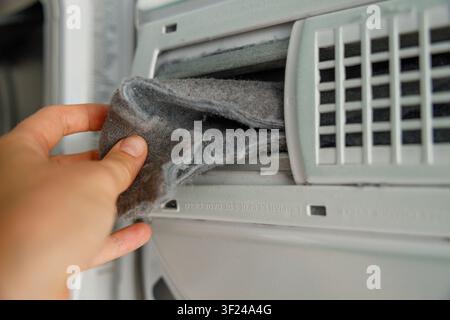 Le dita reggono un grosso batuffolo piegato di lanugine grigia accumulata appena estratto dal filtro dell'asciugatrice, mostrando perché la pulizia regolare è importante per gli elettrodomestici Foto Stock
