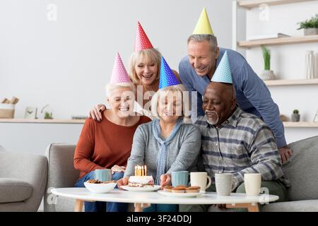 Gruppo diversificato e felice di anziani che celebrano il compleanno con torta e candele a casa, concetto familiare Foto Stock