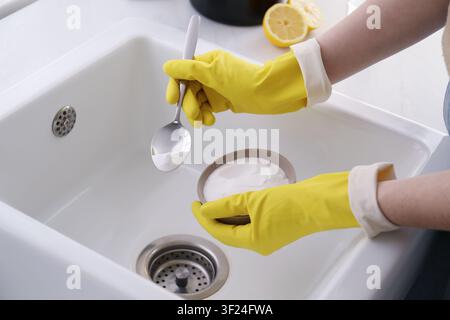 Donna che usa bicarbonato di sodio per disintasare lo scarico del lavandino, primo piano Foto Stock