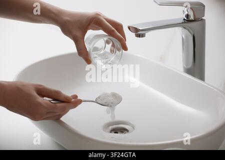 Donna che usa bicarbonato di sodio per disintasare lo scarico del lavandino in bagno, primo piano Foto Stock