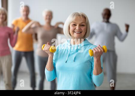 Donna anziana caucasica felice che solleva pesi in una lezione di esercizio, concetto di fitness Foto Stock