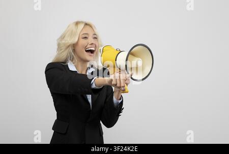 Giovane donna felice che tiene un megafono, indossa un abito nero, concetto aziendale Foto Stock
