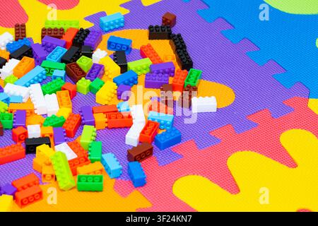 Vista ad angolo alto di molti mattoncini di costruzione in plastica colorati sparsi su uno sfondo luminoso di tappetino puzzle in schiuma Foto Stock