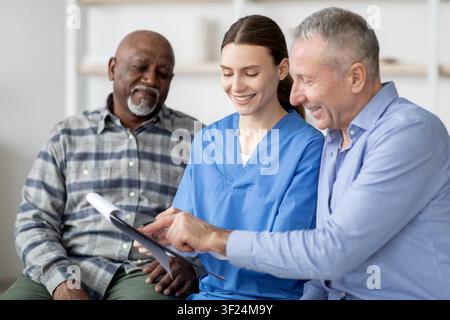 Operatore sanitario sorridente che assiste uomini anziani in clinica, discutendo il piano di trattamento, concetto di assistenza sanitaria Foto Stock
