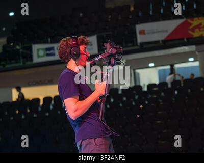 Il videomaker regola una fotocamera professionale montata su un gimbal durante una competizione di breaking. L'immagine cattura il lavoro dietro le quinte di un evento live Foto Stock