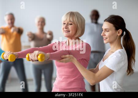 Donna anziana che fa esercizio con i manubri in un ambiente di palestra con un istruttore di fitness, concetto di stile di vita sano Foto Stock