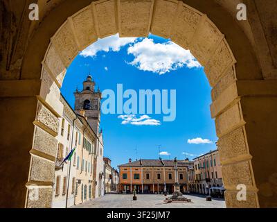 Piazza Ducale storica di Sabbioneta con il campanile e gli edifici antichi in una giornata di sole, vista attraverso un arco di pietra, che trasmette architettura italiana Foto Stock