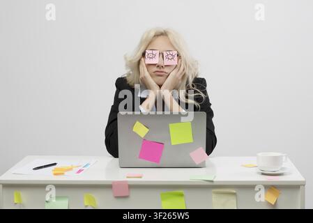Giovane donna caucasica preoccupata che lavora alla scrivania con post-it, concetto di stress lavorativo Foto Stock