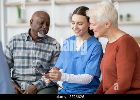 Giovane infermiera sorridente che assiste una coppia caucasica anziana in un contesto sanitario Foto Stock