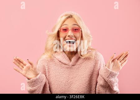 Giovane donna caucasica felice con occhiali da sole che sorride su sfondo rosa Foto Stock
