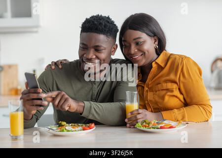 Giovane coppia nera sorridente che gusta la colazione insieme a casa, concetto di alimentazione sana Foto Stock