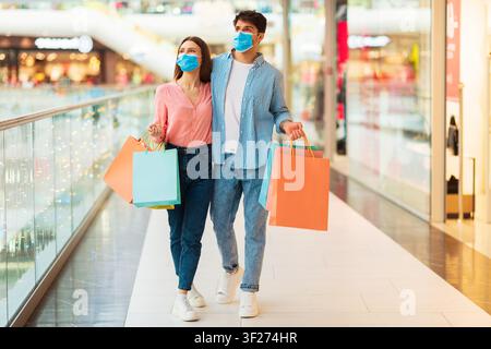 Giovane coppia con borse della spesa e sorridente nel centro commerciale, indossa mascherine, concetto di vendita al dettaglio Foto Stock