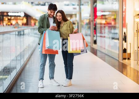 Giova coppia felice con borse della spesa colorate nel centro commerciale, sorridendo insieme Foto Stock