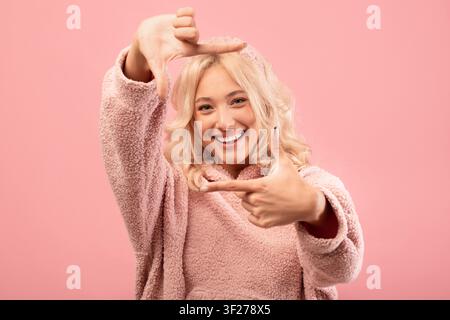 Giovane donna felice che fa un gesto a forma di cornice con le mani, sorridendo, sfondo rosa, ritratto Foto Stock