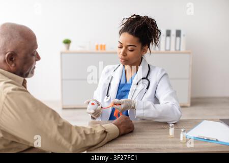 Medico che esamina il polso di un paziente maschio nero anziano in un contesto sanitario, azione focalizzata Foto Stock