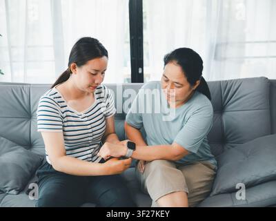 Madre asiatica e figlia adulta che controllano il tracker sanitario dello smartwatch sul divano a casa, concetto di tecnologia indossabile, cura familiare, assistenza sanitaria digitale, w Foto Stock