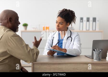 Medica donna che consulta un paziente maschile nero anziano in un ambiente sanitario Foto Stock