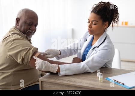 Paziente anziano maschio di colore che riceve una vaccinazione da un'infermiera in una clinica, concetto di assistenza sanitaria Foto Stock