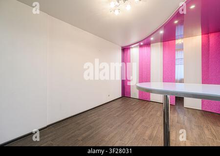 stanza con pareti bianche, pavimento in legno marrone e dettagli a righe rosa e bianche. Un tavolo si trova nell'angolo Foto Stock