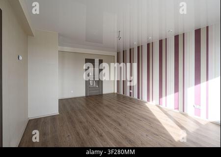 Stanza luminosa e vuota con pavimenti in legno, carta da parati a righe e una porta moderna. La luce entra evidenziando il design pulito e minimalista Foto Stock
