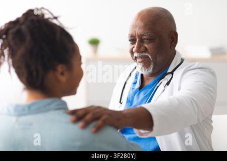 Medico nero sorridente che consulta con un paziente in clinica, concetto di assistenza sanitaria Foto Stock