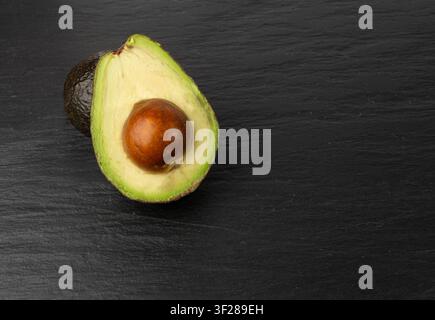 Mezza avocado Hass, set completo Sharwil, avocado marroni tagliati, pera alligatore fresca, ingrediente per guacamole, frutto di avocado Persea Americana su sfondo nero Foto Stock