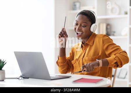 Donna nera felice con cuffie che si gode un corso online a casa, concetto di educazione Foto Stock