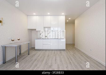 Cucina luminosa e moderna con armadi bianchi, pavimenti in legno chiaro e un tavolino Foto Stock