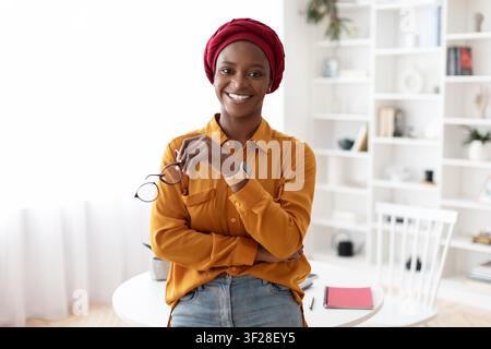 Donna nera sorridente con occhiali in piedi in un ufficio domestico, concetto di business Foto Stock