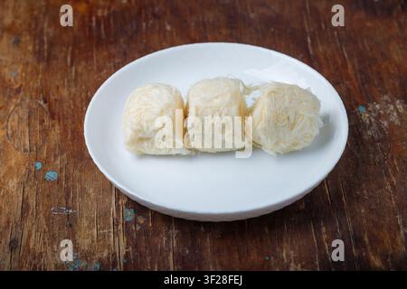 Pismaniye, zucchero filato o barba di drago con gusto di vaniglia su piatto bianco, sfondo di legno. Dessert turco, halva leggera, zucchero filato. Spazio di copia Foto Stock