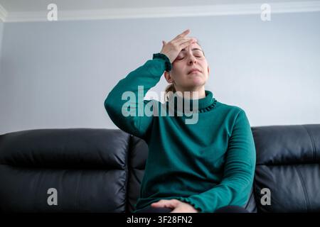 Donna che sente dolore per mal di testa o emicrania, seduta sul divano a casa Foto Stock