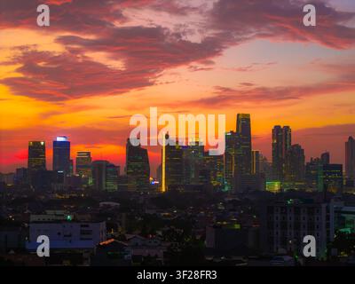 Vista aerea dello skyline di Jakarta al tramonto con grattacieli illuminati e nuvole vibranti arancioni e viola sulla città, Tebet, Jakarta, Indonesia Foto Stock