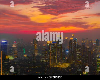 Vista aerea dello skyline di Jakarta al tramonto con grattacieli illuminati e nuvole arancioni vibranti sulla città di Tebet, Jakarta, Indonesia. Foto Stock