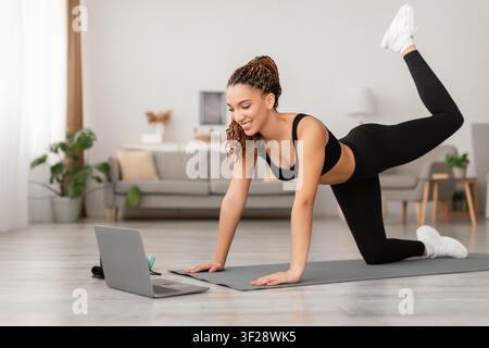 Giovane donna nera felice che si allena a casa, utilizza un laptop, concetto di esercizio fisico Foto Stock