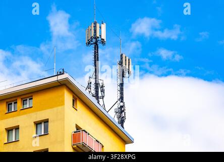 Antenne di rete cellulare mobile e trasmettitori di telecomunicazione installati sul tetto di un edificio residenziale giallo contro un cielo blu Foto Stock