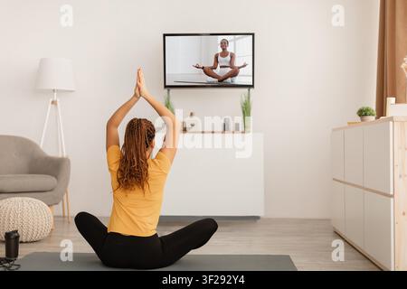 Yogini afroamericana che pratica la meditazione a casa con un istruttore online. Concetto di benessere Foto Stock