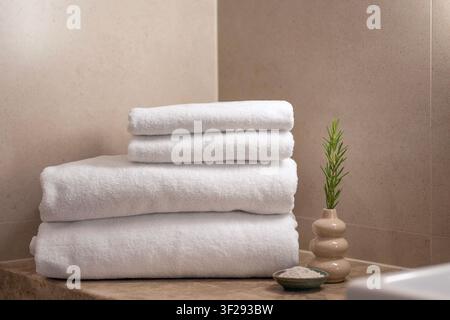 Asciugamano bianco arrotolato su un vassoio da bagno in legno con articoli per il benessere in un bagno moderno di hotel, creando un'atmosfera rilassante di benessere Foto Stock
