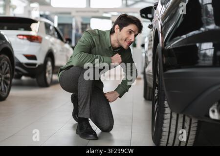 Giovane uomo concentrato che ispeziona un pneumatico dell'auto in un concessionario, concetto aziendale Foto Stock