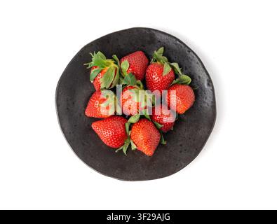 Fragola fresca isolata, mucchio di fragole rosse mature su piatto nero, fragola rossa succosa imperfetta con foglie verdi, fragola naturale deliziosa Foto Stock