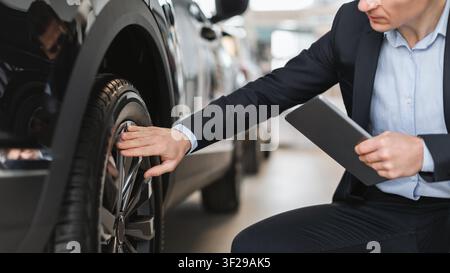 Uomo d'affari che controlla la pressione delle gomme su un'auto in un concessionario automobilistico, ambiente professionale Foto Stock
