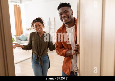 Giovane coppia nera sorridente in piedi sulla porta che accoglie gli ospiti, ambiente domestico Foto Stock