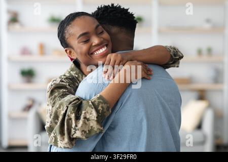 Soldato nera felice che abbraccia il partner maschile a casa, concetto di riunione emotiva Foto Stock