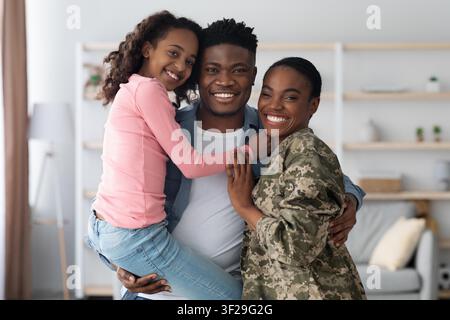 Famiglia afroamericana felice insieme a casa, abbracciandosi e sorridendo Foto Stock