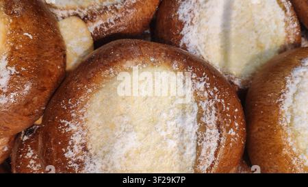 Una vista ravvicinata di panini dorati cotti al forno, ripieni di formaggio fresco e leggermente spolverati di zucchero a velo. Foto Stock