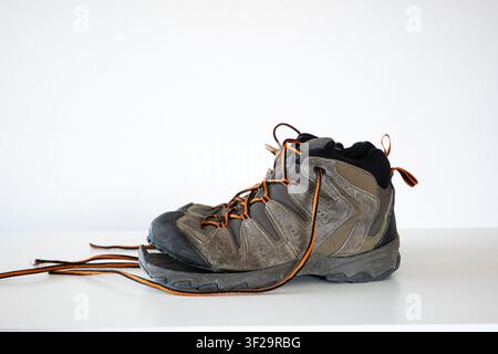 Uno scatto laterale in studio di un paio di vecchie scarpe da trekking consumate che mostrano una suola di gomma rotta e staccata all'altezza delle punte con lacci arancioni su uno sfondo bianco pulito Foto Stock