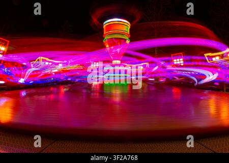 Vista di un'attrazione da luna park in rotazione di notte catturata con esposizione lunga che crea vivaci tracce di luce viola e rosse ad Almere, Flevoland, Paesi Bassi Foto Stock