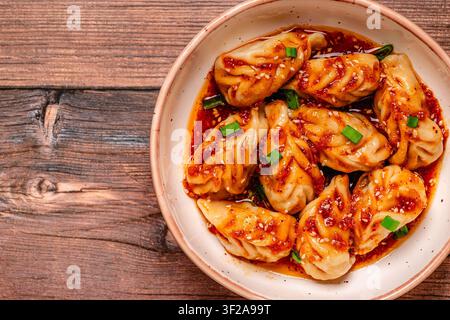 Deliziose gnocchi serviti in una ciotola con una salsa piccante e cipollotti su un tavolo di legno Foto Stock